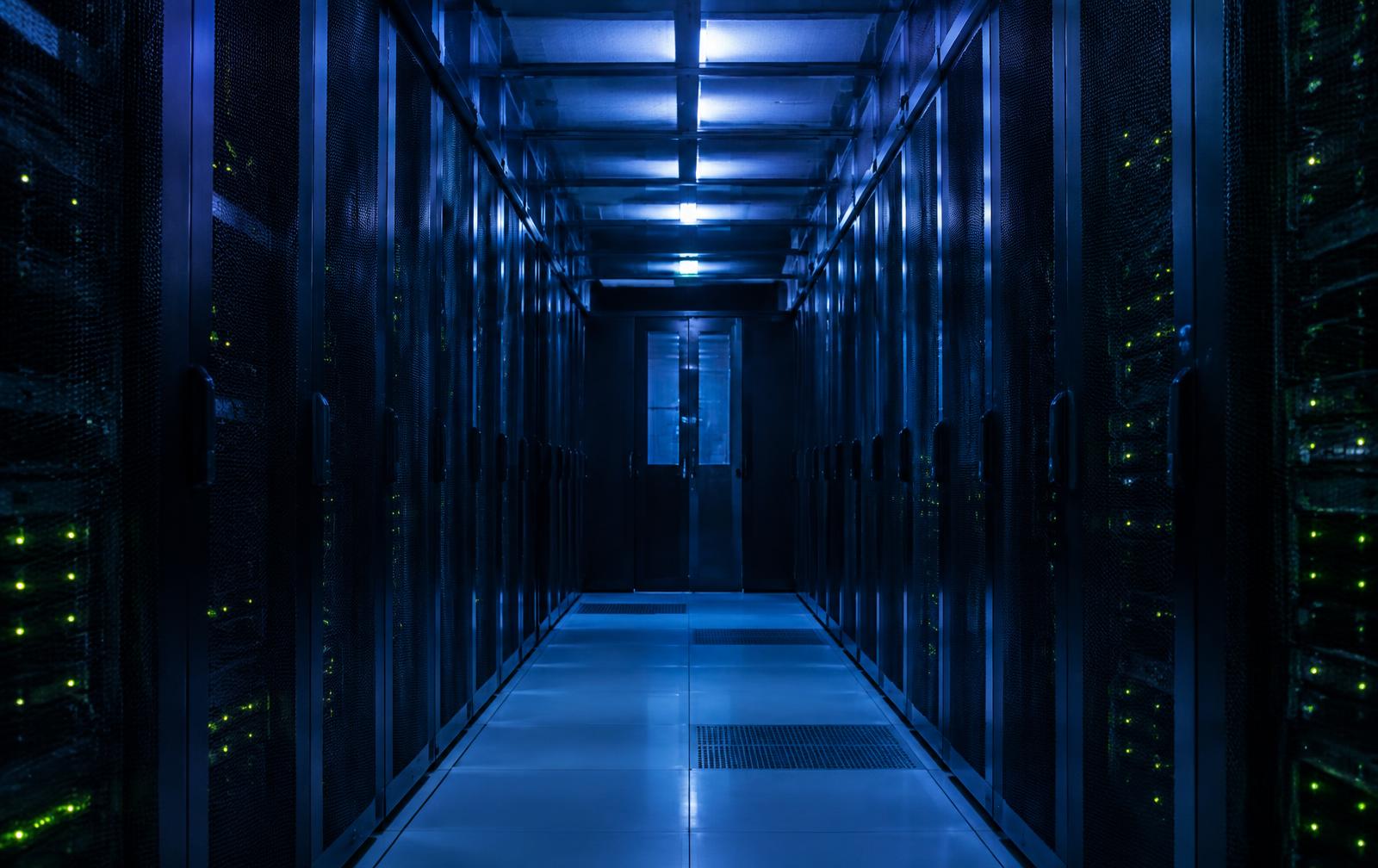 Server racks in a data centre corridor under cool blue lighting